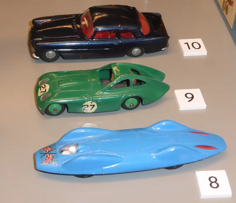 Three die-cast model cars in navy, green and blue, each with a numbered label, on a display shelf