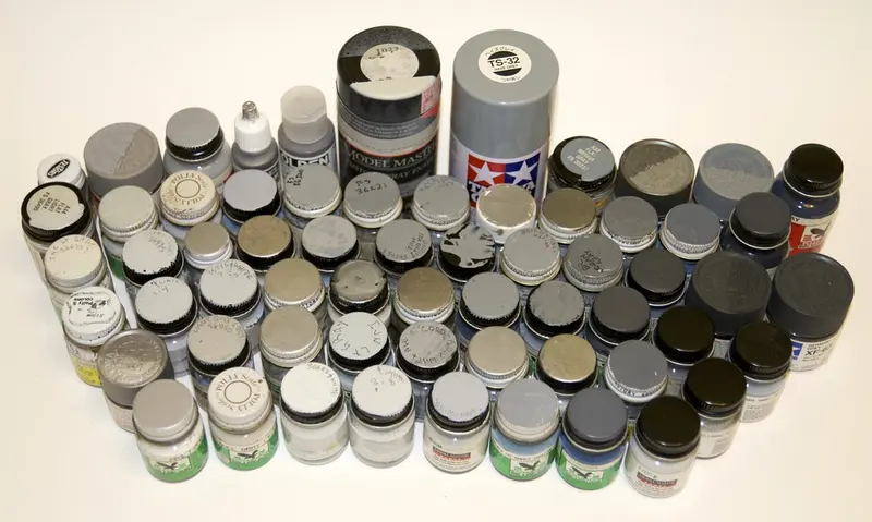 Dozens of small pots of grey and neutral model paints arranged on a white table