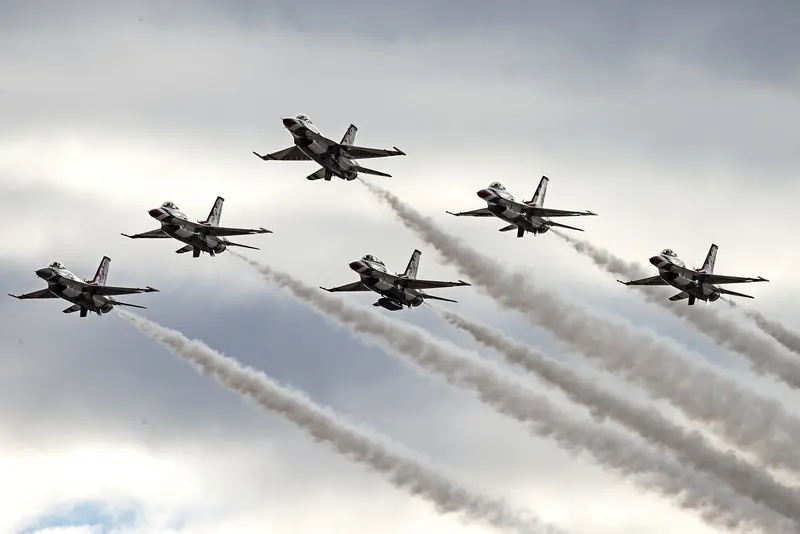 Six F-16 jets trailing white smoke against a grey sky