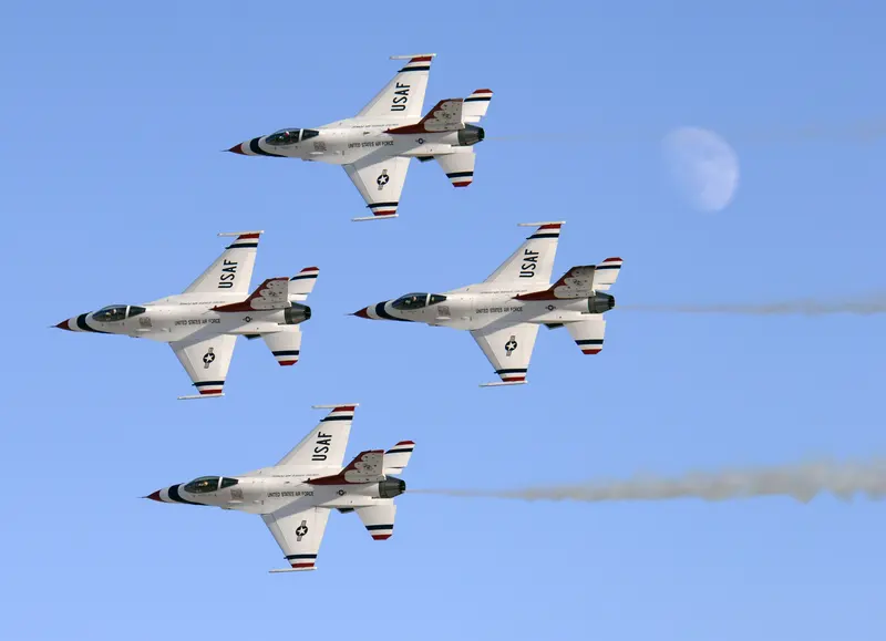 Four Thunderbirds F-16s in diamond formation against a blue sky with the moon visible