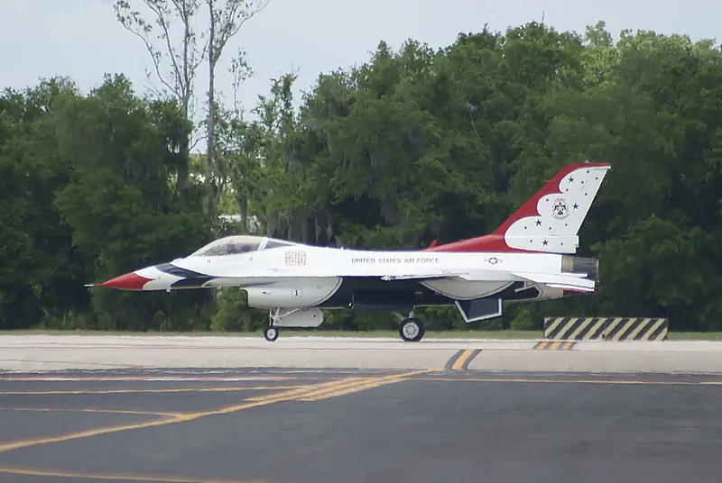 A white, red and blue USAF Thunderbirds F-16C, aircraft number 1, taxiing past trees