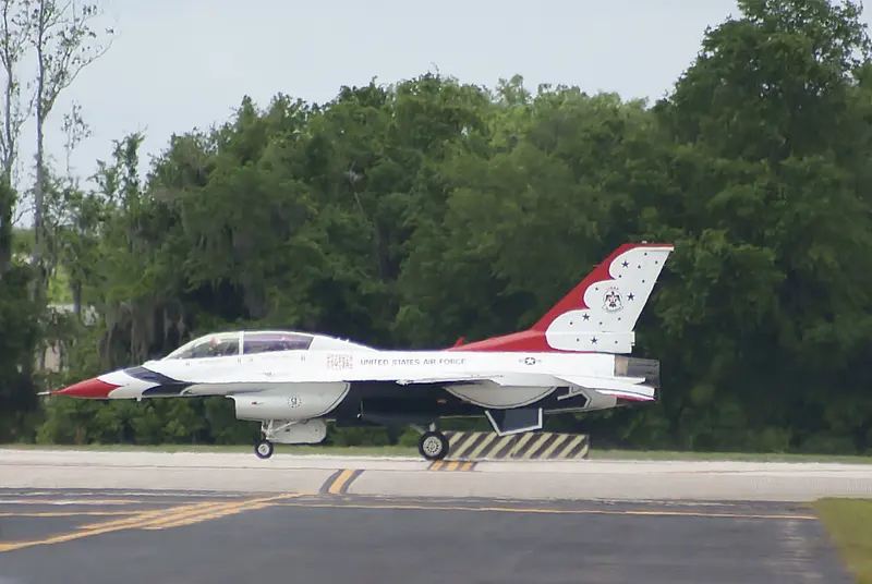 A Thunderbirds F-16C, aircraft number 5, taxiing along a runway lined with trees
